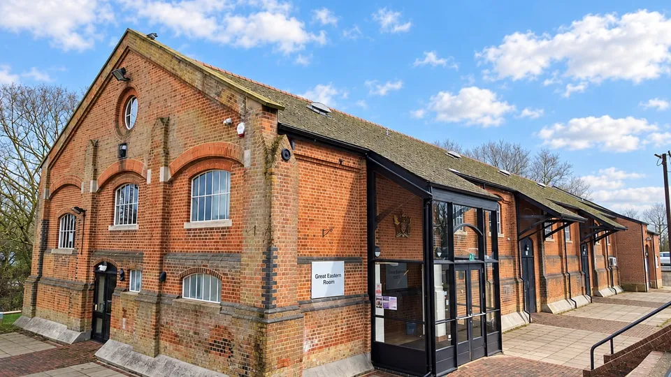 The Freight House under a blue sky: a long red-brick Victorian goods shed with a slate roof and a round window in the gable, with a modern glazed entrance porch on the side facing the car park.