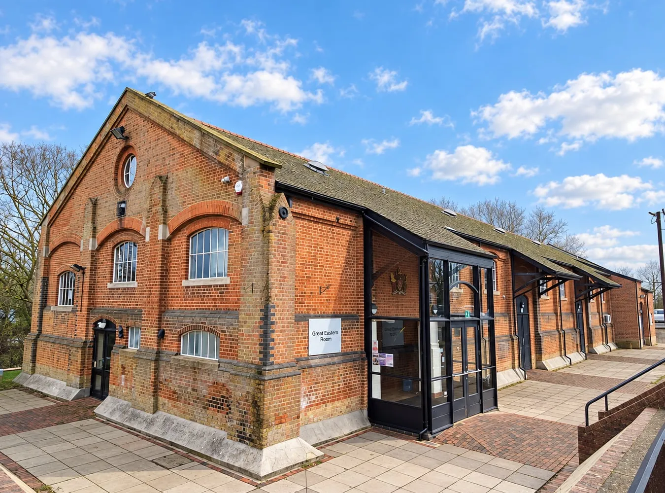 The Freight House under a blue sky: a long red-brick Victorian goods shed with a slate roof and a round window in the gable, with a modern glazed entrance porch on the side facing the car park.