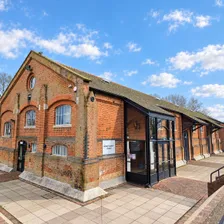 The Freight House under a blue sky: a long red-brick Victorian goods shed with a slate roof and a round window in the gable, with a modern glazed entrance porch on the side facing the car park.